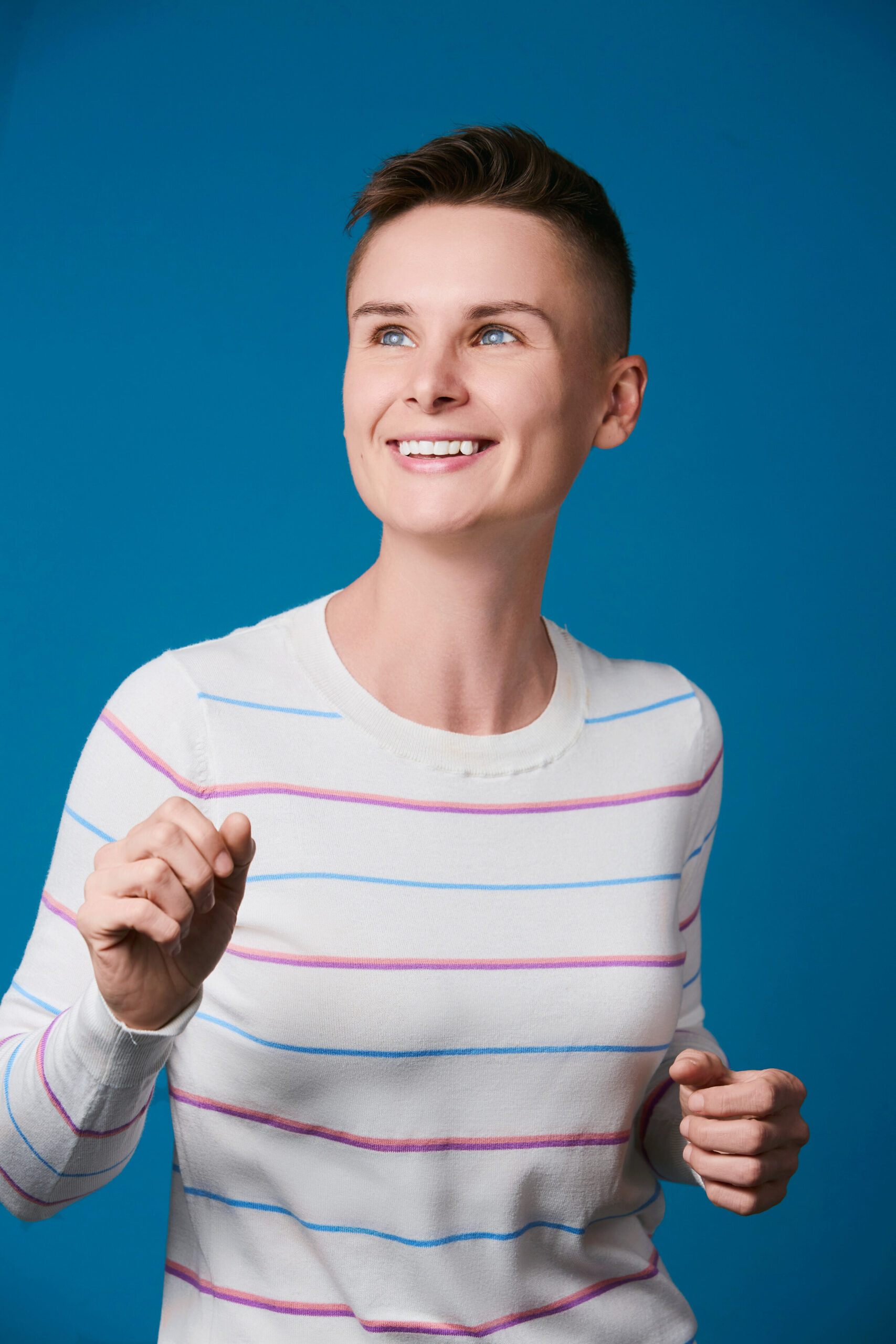 Female comedian Ashley G for hire in a stripped shirt smiling.