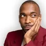 Comedian Jay Pharoah with maroon sports coat and hand on his face in front of a white background.