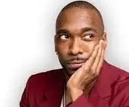 Comedian Jay Pharoah with maroon sports coat and hand on his face in front of a white background.