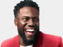 Kevin Hart Comedian smiling with a red suit on in front of a gray background.