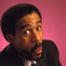 Comedian Richard Pryor with a suit on with a light red background.
