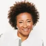 Comedian Wanda Sykes smiling with white jacket in front of a white background.