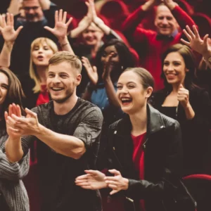 Crowd of people clapping and smiling at a comedian for hire.