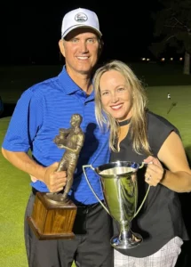 Corporate Motivational Speaker for hire Ron Nanney wearing a white Warwick Hills cap and blue polo holding a bronze trophy next to a blond woman in a black tank top holding gold trophy standing on a golf course.