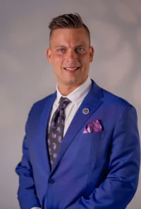 Business and Corporate Sales Motivational Speaker for hire Ryan Listerman in a blue suit with short dark blonde hair.