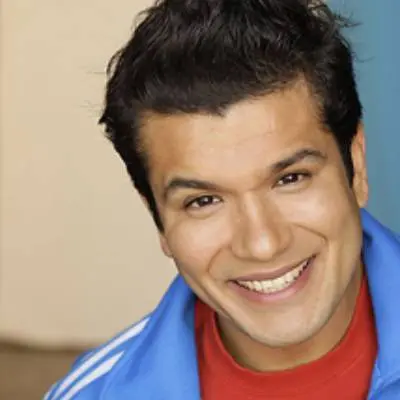Male Hispanic Comedian for hire in blue jacket and red t-shirt.