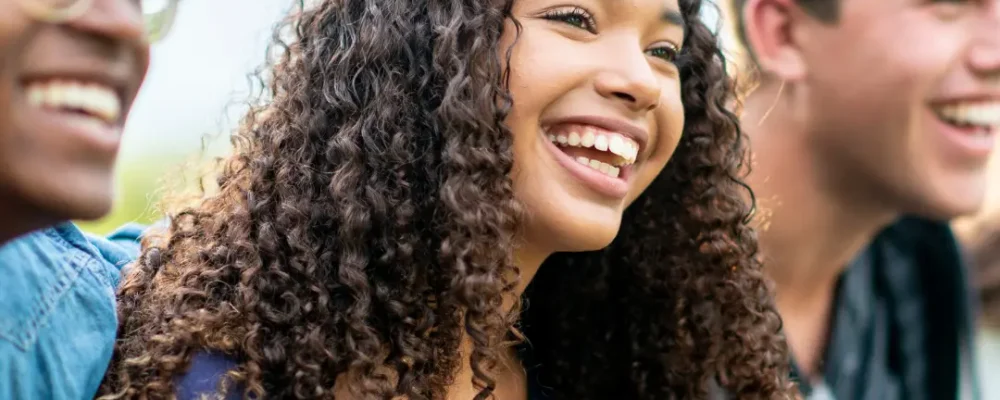 Three young people- black male with glasses, black female with long hair and a white male with blond hair laughing at a Christian comedian.