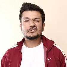 Hispanic comedian Robert Zapata in a red jacket and white shirt making a snarl face.