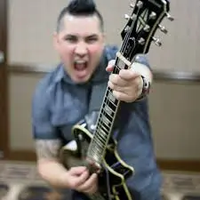 Hispanic comedian for hire Ace Guillen holding guitar out toward the camera.