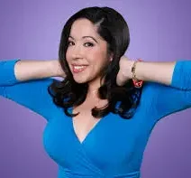 Hispanic comedian Gina Brillon in a blue blouse and purple background.
